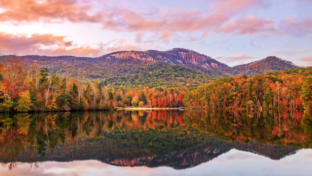 Un lac paisible qui reflète une chaîne de montagnes boisée, dont le feuillage arbore les couleurs de l’automne.