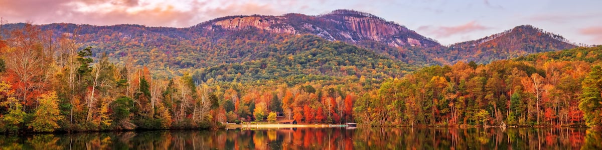 A calm lake reflecting a forested mountain range with autumn foliage.