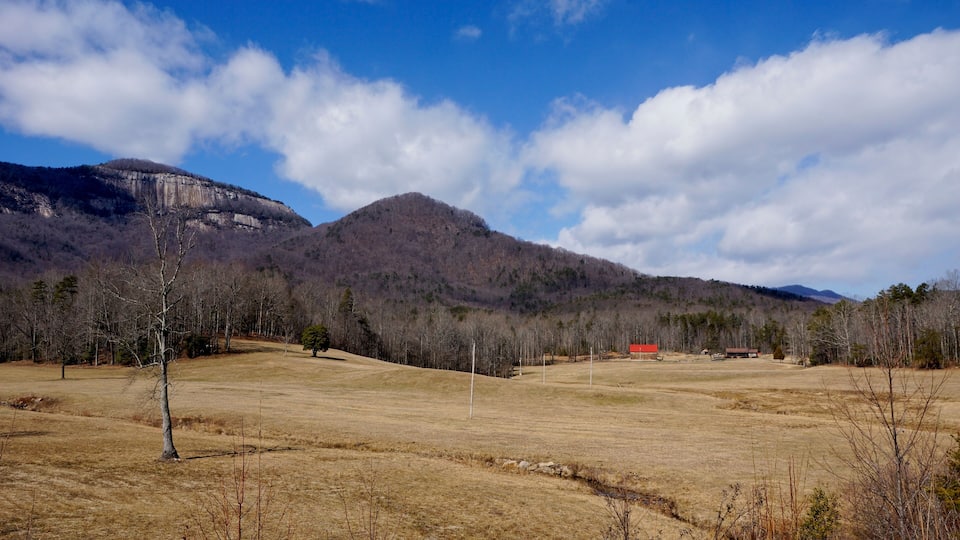 A dry grassland with a few trees, a red building, and mountains in the background.