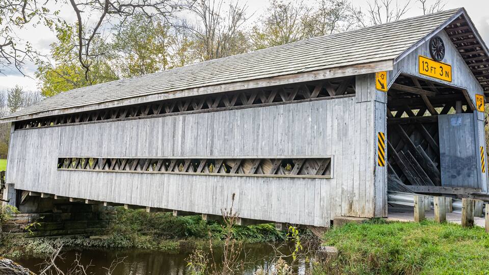 A covered wooden bridge with a height restriction sign of 13 ft 3 in.