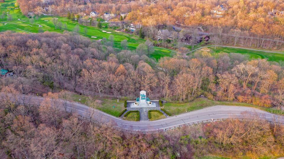 An aerial view of a golf course with a monument in the center, surrounded by trees and residential houses.