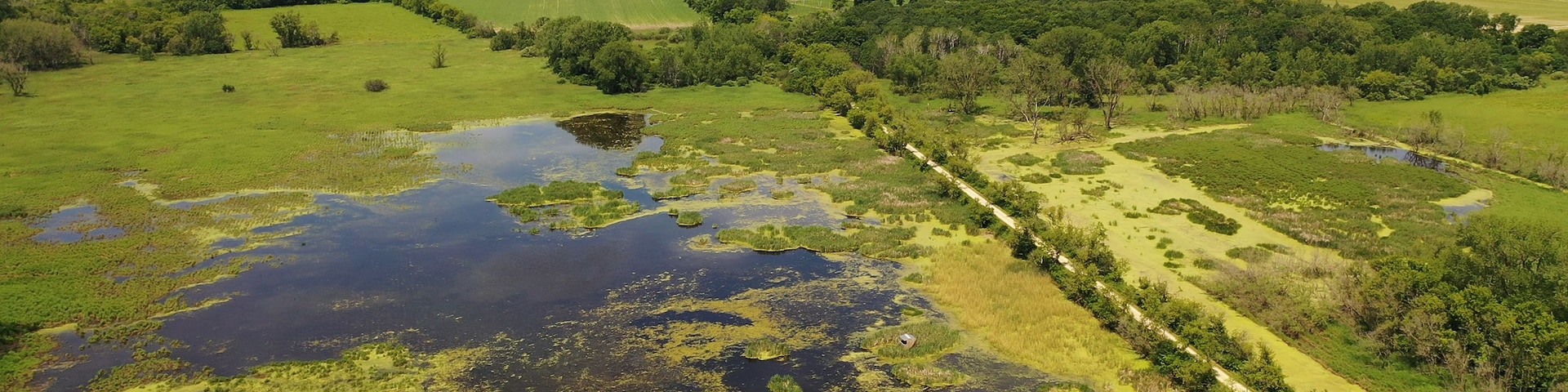 Eine ländliche Landschaft mit einer weiten Feindesumgebung, einer unbefestigten Straße und verstreuten Gebäuden in der Ferne.