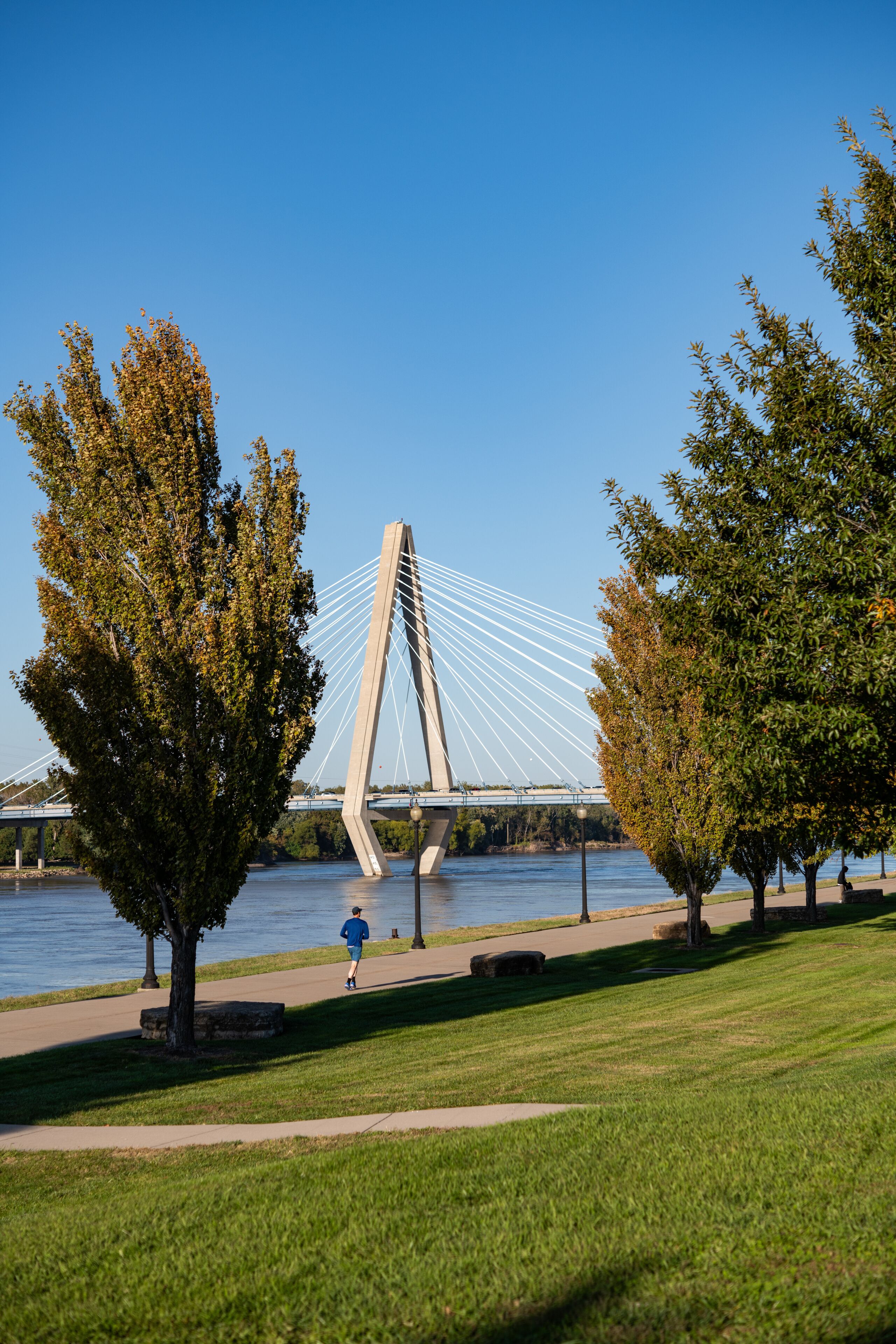 Adult man running on riverfront greenway with bridge in background 