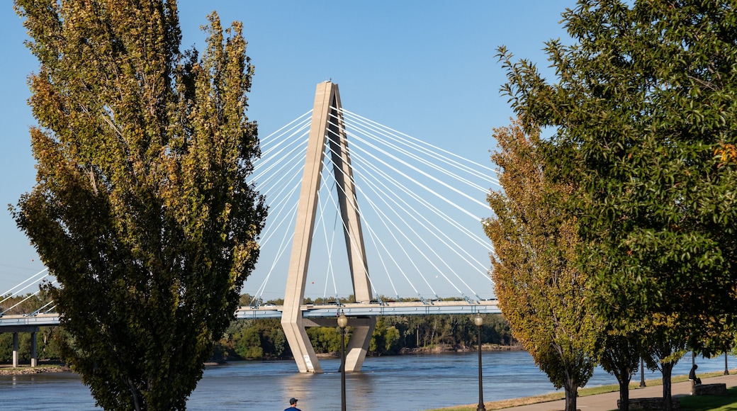 Adult man running on riverfront greenway with bridge in background