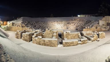 An ancient amphitheater with stone seating and a snow-covered landscape.