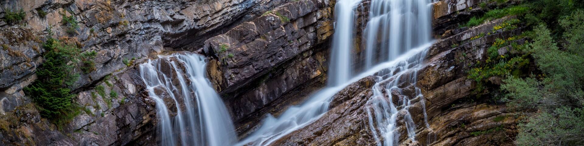 A multi-tiered waterfall cascading down a rocky cliff into a river.