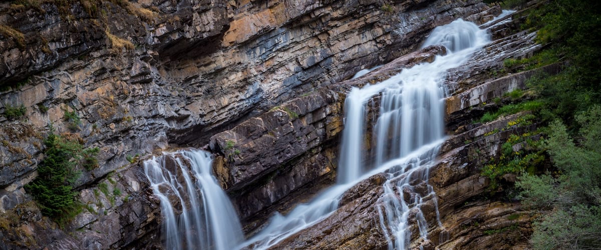 A multi-tiered waterfall cascading down a rocky cliff into a river.
