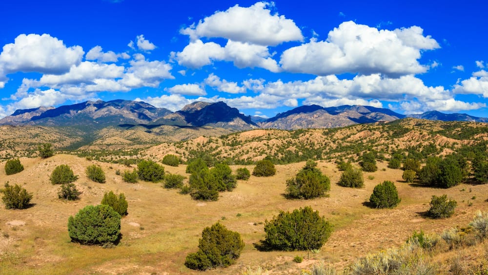 A mountainous landscape with scattered green trees and a clear blue sky.