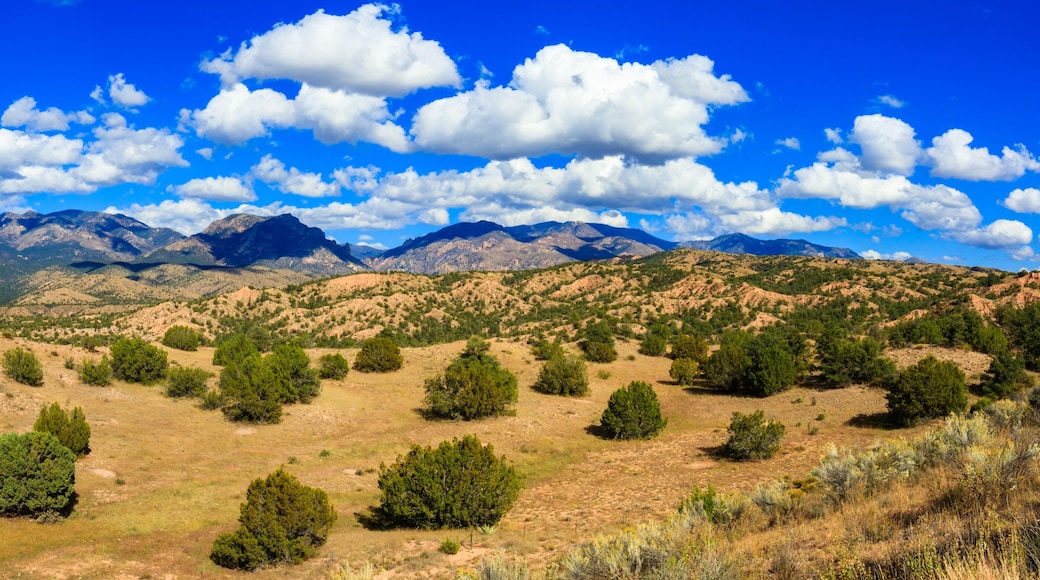 A mountainous landscape with scattered green trees and a clear blue sky.