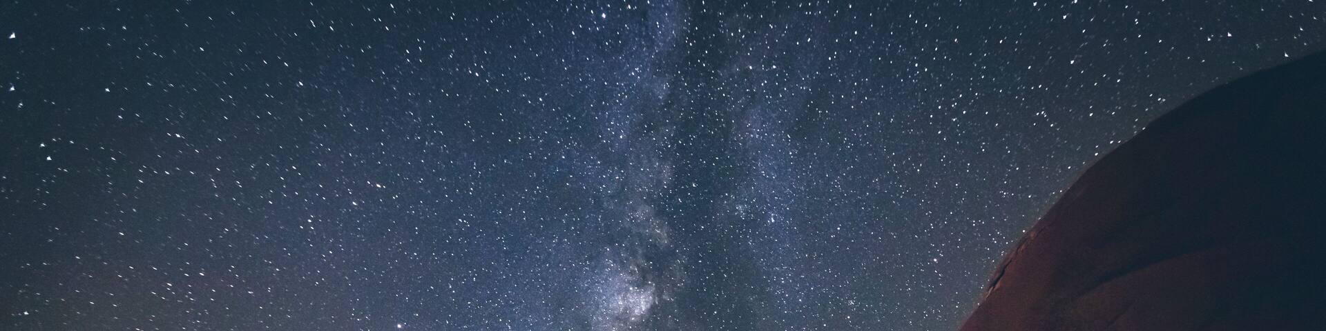 A night sky with stars and the Milky Way over rock formations.