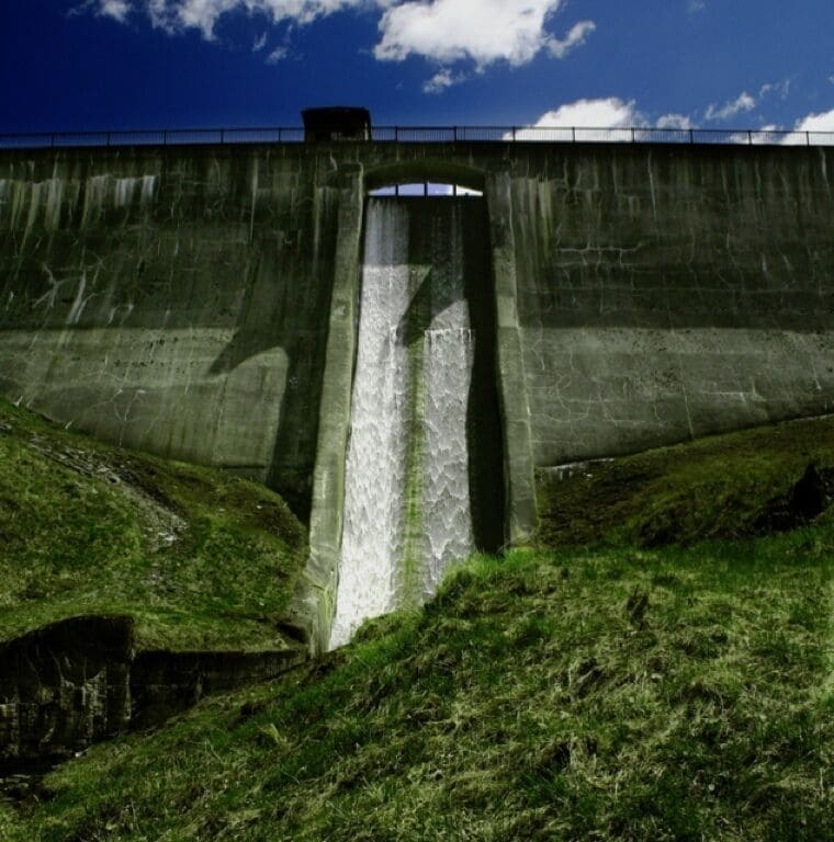 A concrete dam with a water spillway and grassy banks.