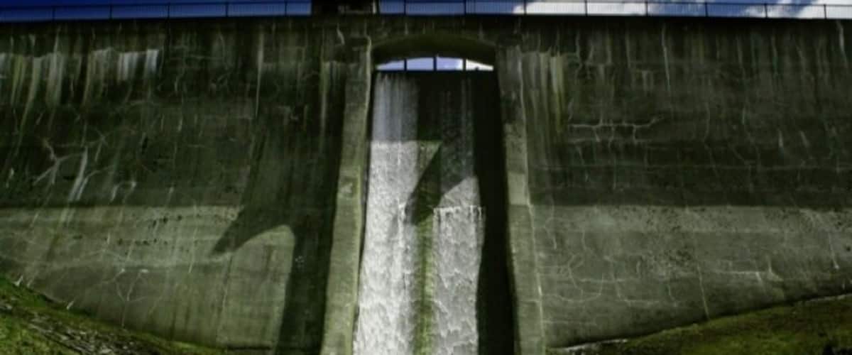 A concrete dam with a water spillway and grassy banks.