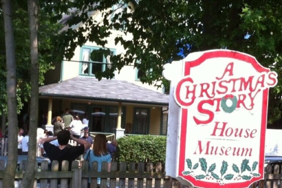 A Christmas Story House Museum sign with a wooden fence and trees in the background.