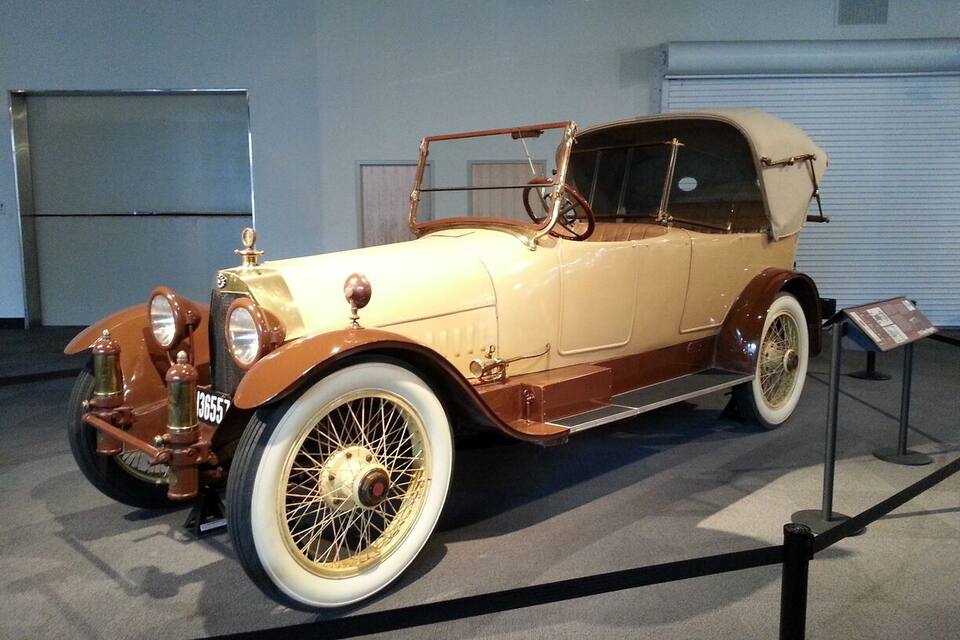 A vintage car on display with a beige body, white wheels, and a brown front grille.