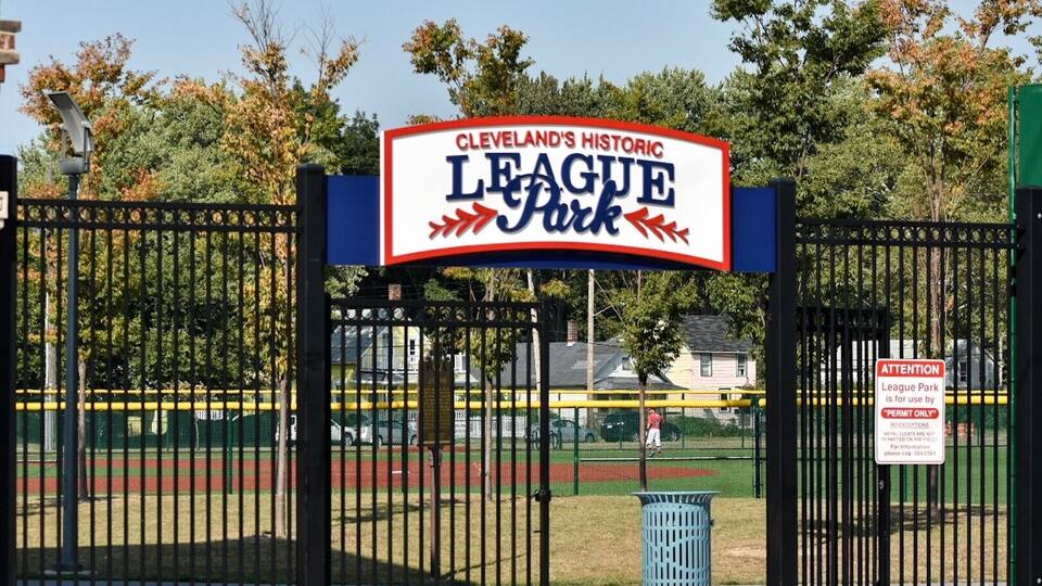 A sign for Cleveland's Historic League Park with a baseball field in the background.