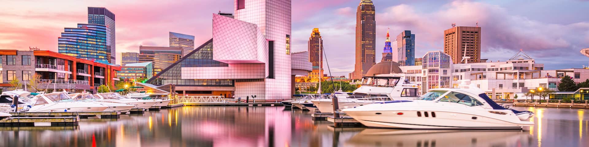 A marina with yachts, a modern city skyline, and a pink and purple sky.