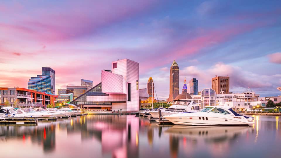 A marina with yachts, a modern city skyline, and a pink and purple sky.