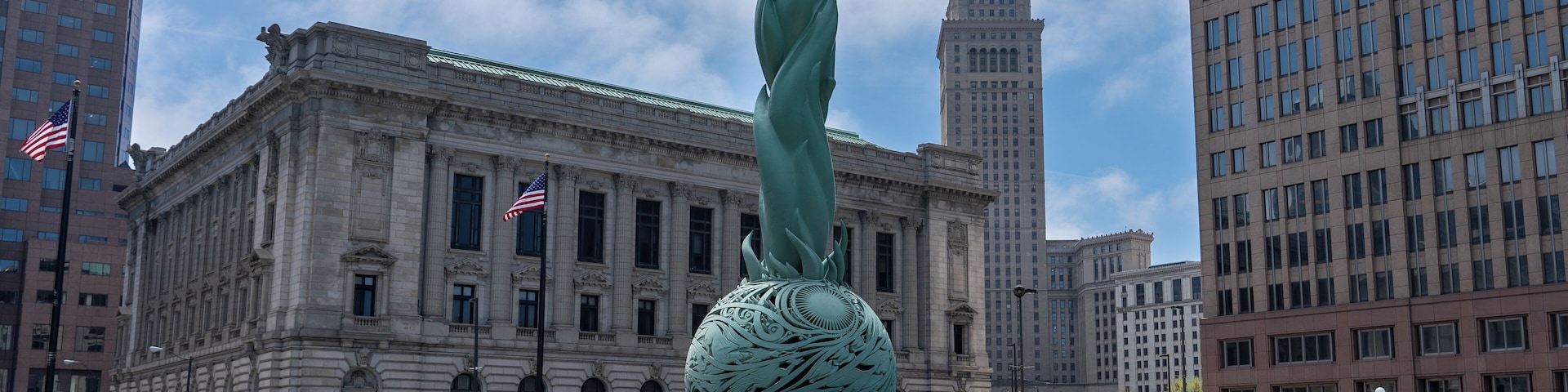 Eine Statue einer Frau mit erhobenen Armen, eine große dekorative Kugel und ein Brunnen vor einem historischen Gebäude mit amerikanischen Flaggen.