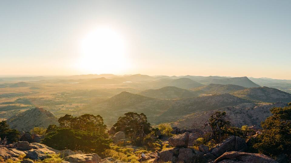 A mountainous landscape with a clear sky and the sun shining.