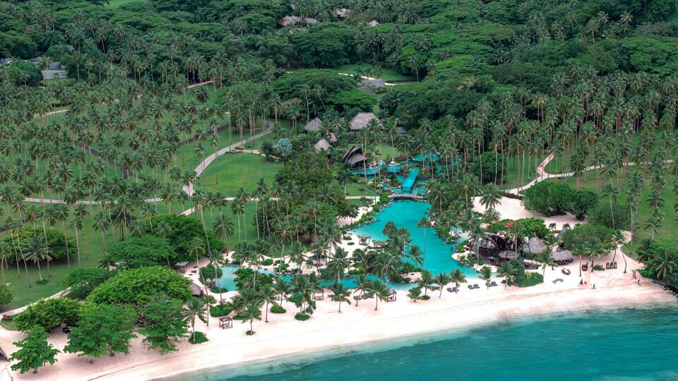 A tropical resort with a turquoise pool, palm trees, and a beach.