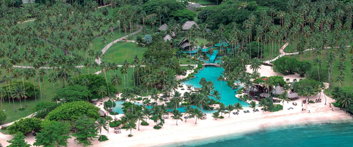 A tropical resort with a turquoise pool, palm trees, and a beach.