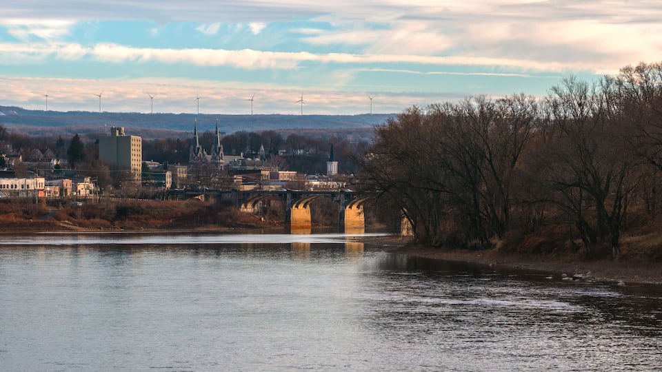 A river with a bridge, a town with buildings, and wind turbines in the background.