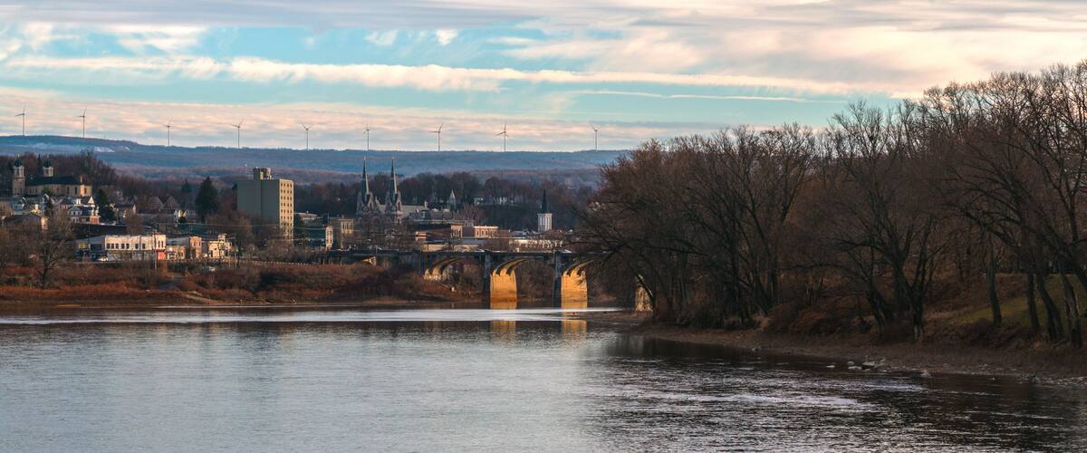 A river with a bridge, a town with buildings, and wind turbines in the background.