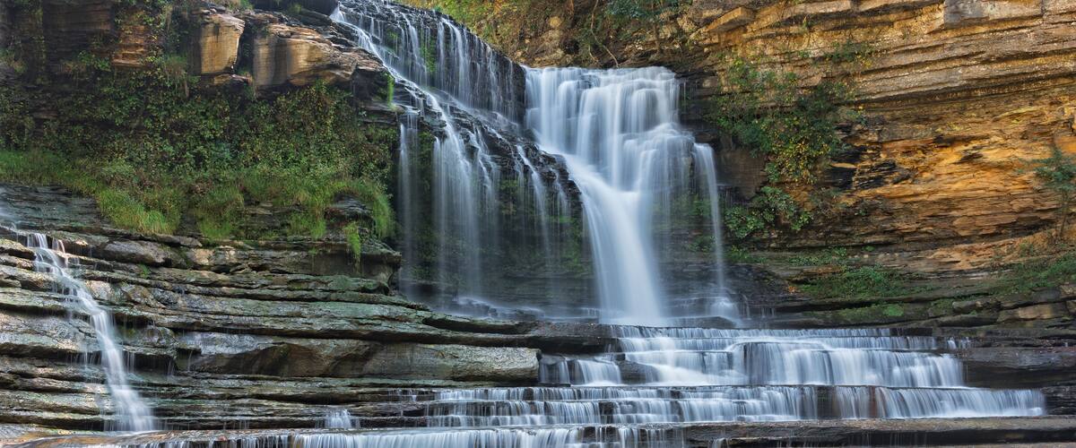 A multi-tiered waterfall cascading over rocky cliffs into a calm pool.