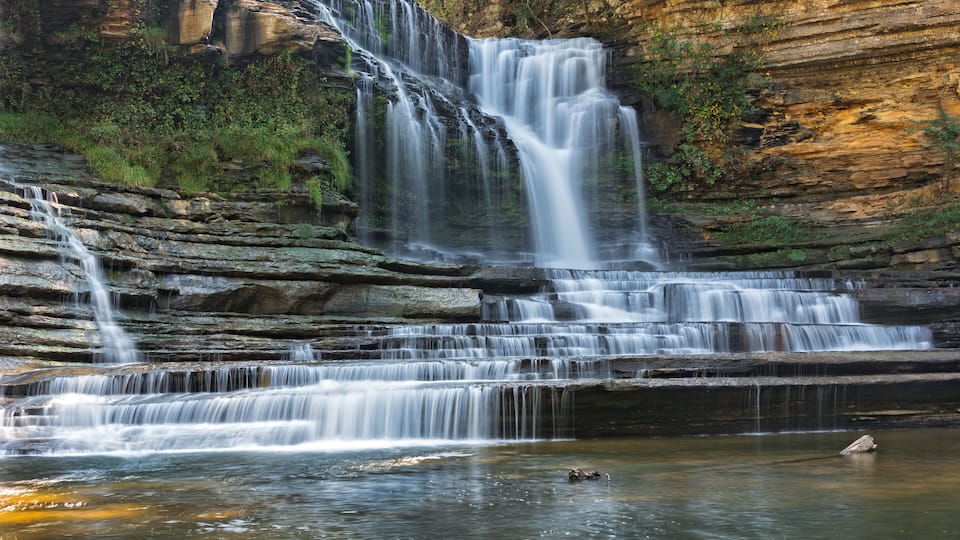 A multi-tiered waterfall cascading over rocky cliffs into a calm pool.