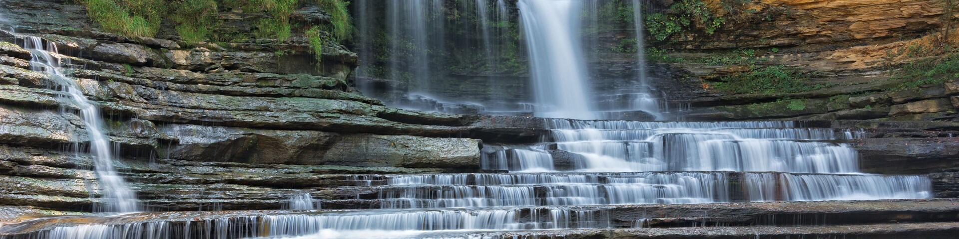 A multi-tiered waterfall cascading over rocky cliffs into a calm pool.