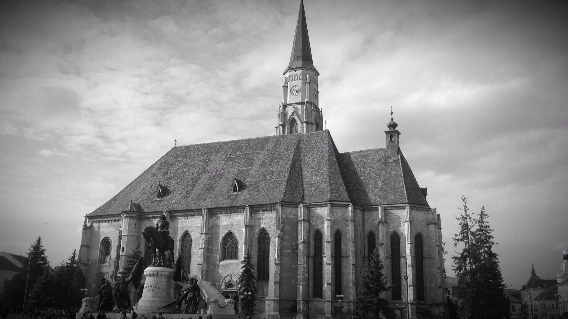 A historic church with a tall spire, a clock tower, and statues in front.