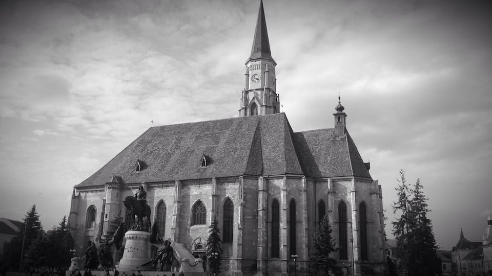 A historic church with a tall spire, a clock tower, and statues in front.