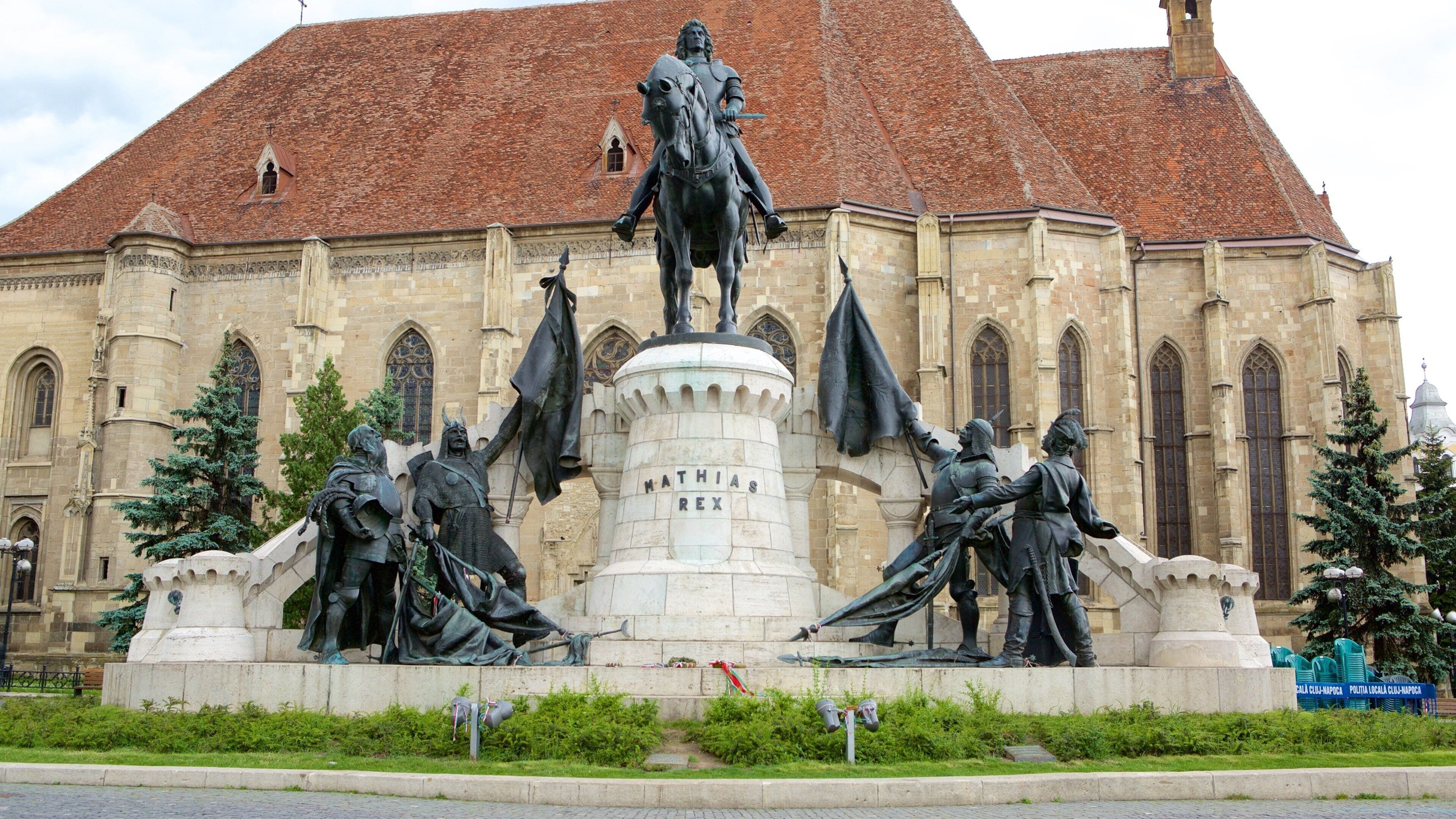 A historical statue of a figure on horseback in front of a large building with a red-tiled roof.