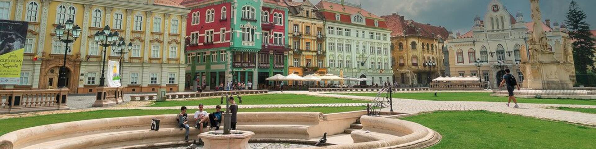 A historic square with colorful buildings, a fountain, and a statue.