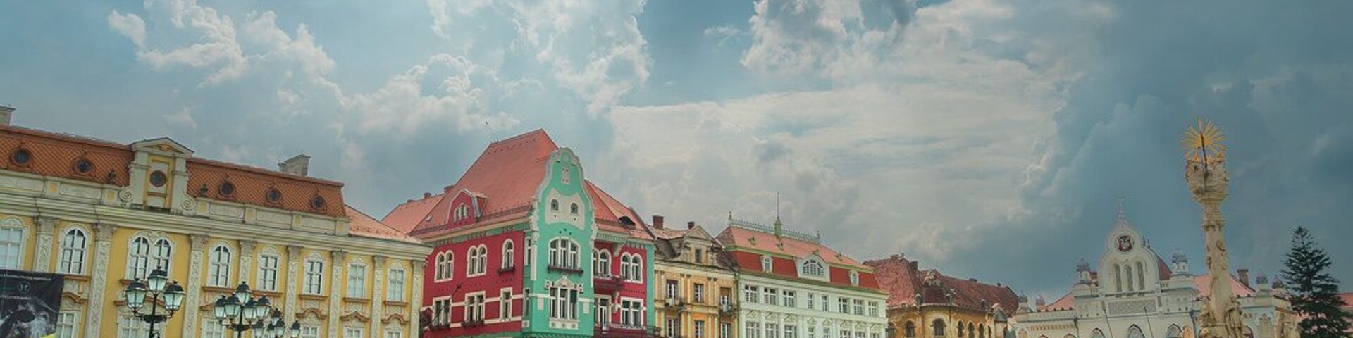 Uma praça histórica com edifícios coloridos, uma fonte e uma estátua.
