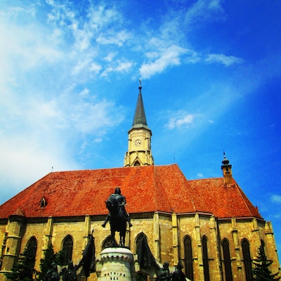 Eine Kirche mit rotem Dach, einem Glockenturm und Statuen davor.
