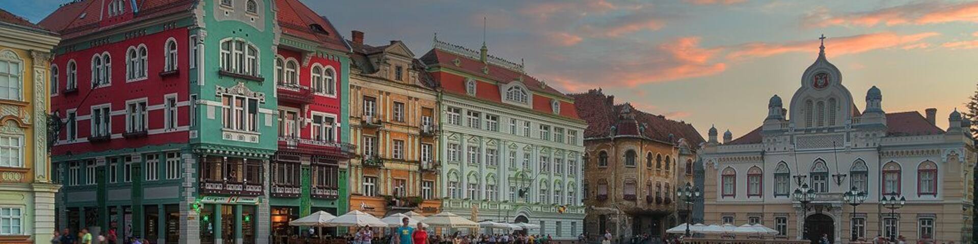 A historic square with colorful buildings, cobblestone paths, and a large open lawn.