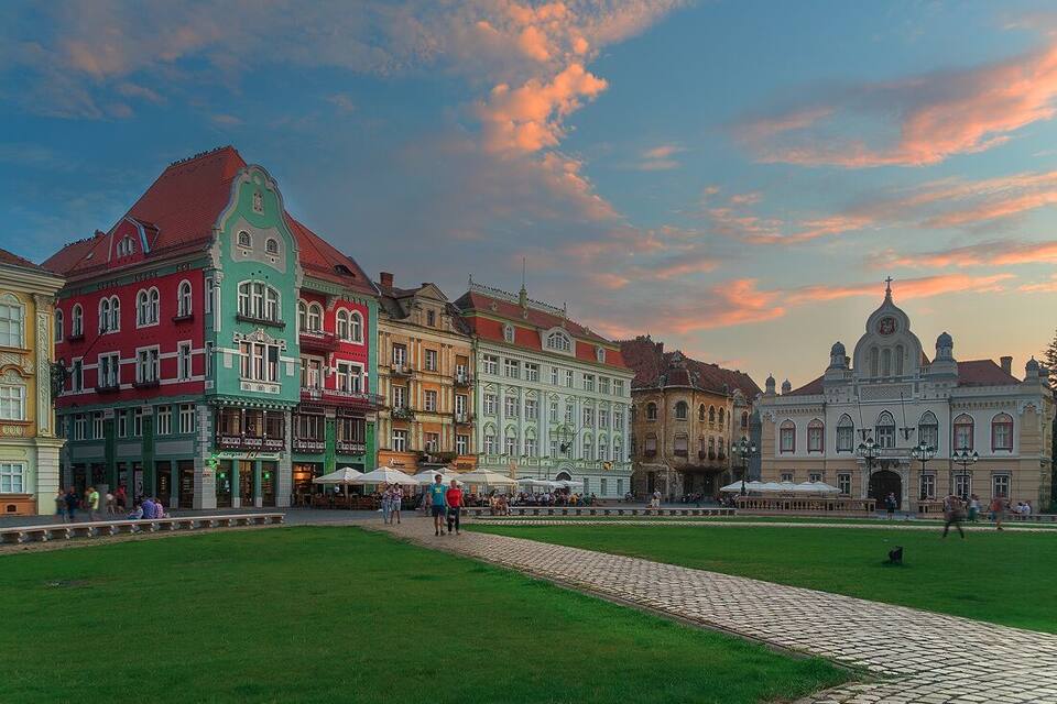 Una plaza histórica con edificios coloridos, caminos empedrados y un amplio césped.
