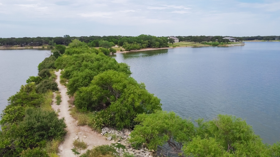 Top view lush green hiking trail lead to the lakeside neighborhood with upscale two story house in Lakewood Village, Texas, America