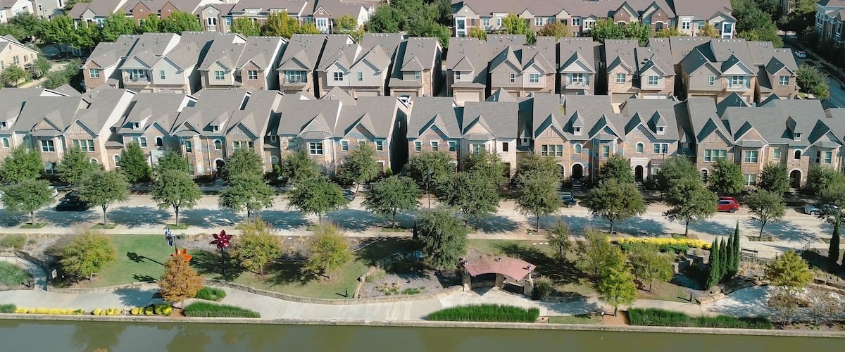 Panorama aerial townhouses arranged symmetrically along central driveway, with canal-side walkways and landscaped trees, suburban density and organized residential planning, Flower Mound, TX