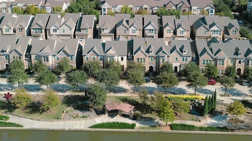 A residential area with houses, trees, a small body of water, and a bridge.