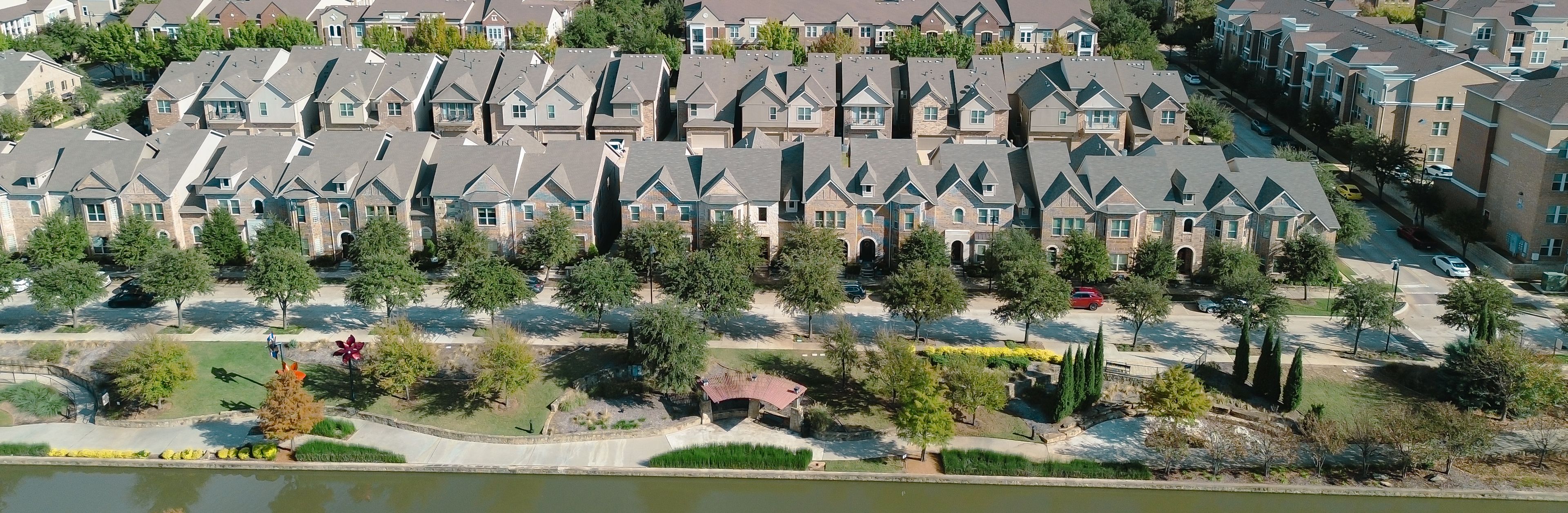 A residential area with houses, trees, a small body of water, and a bridge.