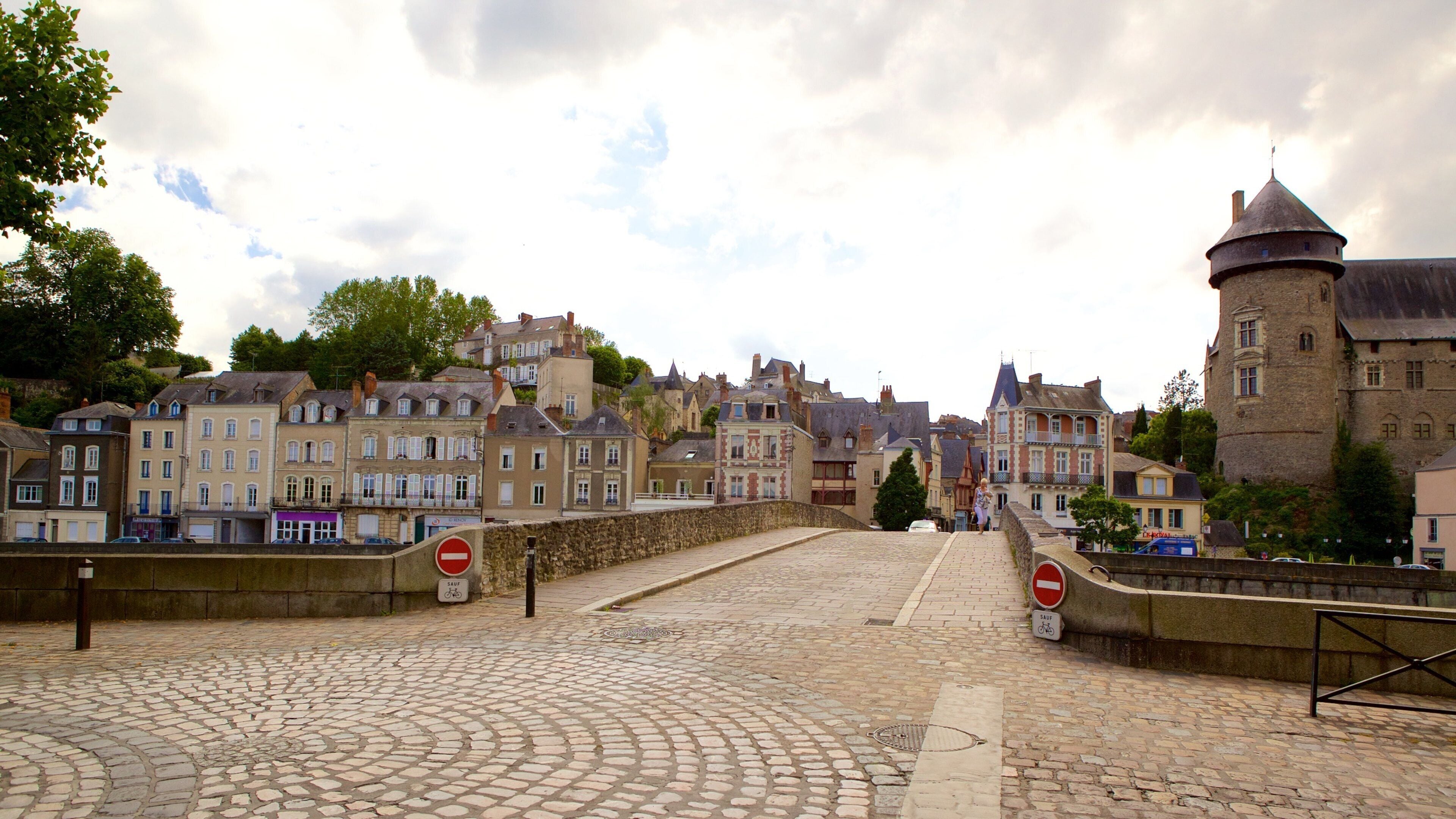 A cobblestone street leading to a historic town with old buildings and a tower.