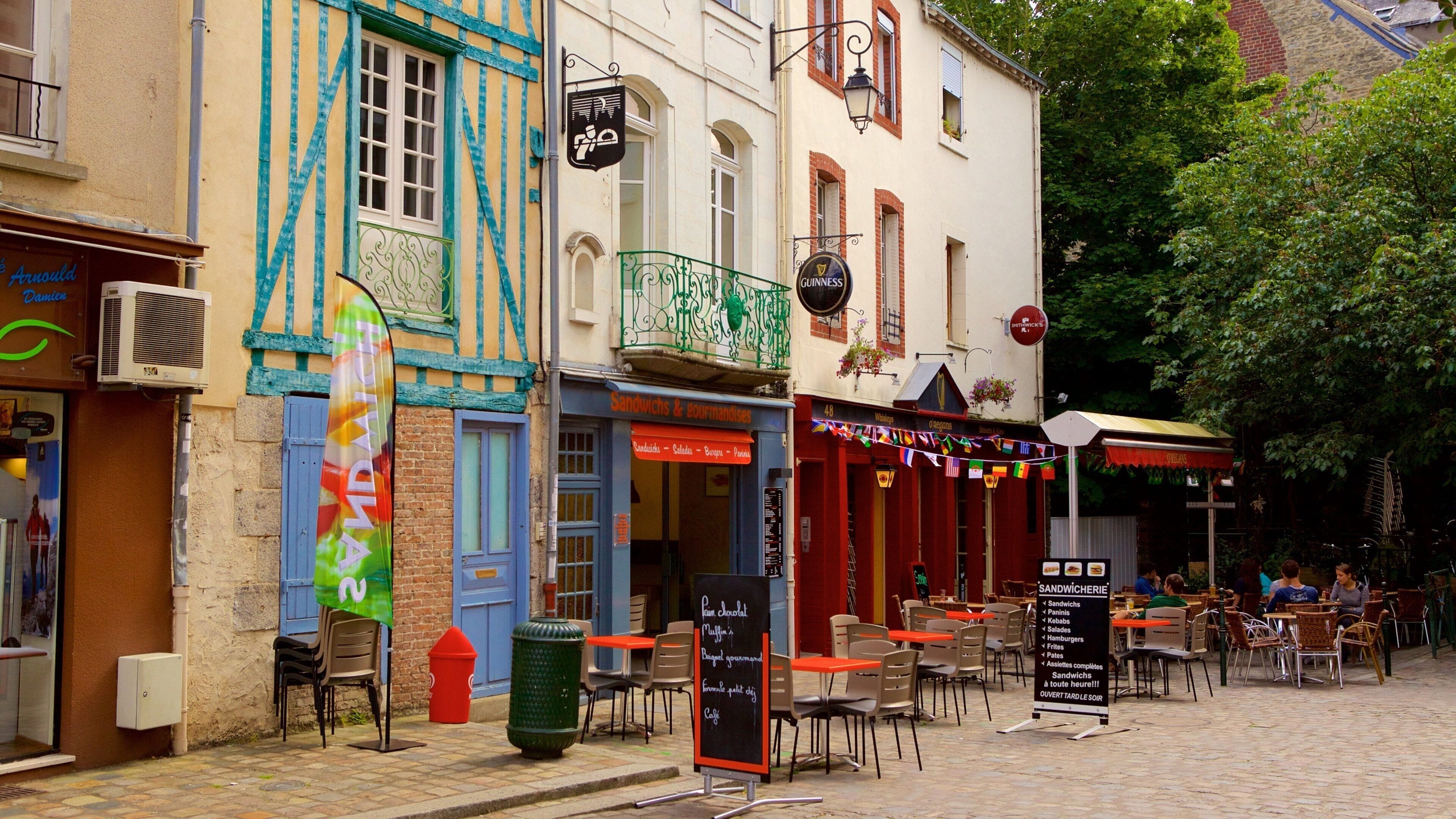 A cobblestone street with outdoor seating at cafes, a sign for 'Sandwiches & gourmandises', and a 'Guinness' sign above a pub.