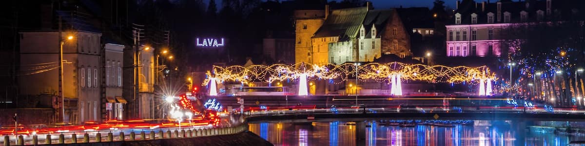 A nighttime cityscape with illuminated buildings, a bridge, and a river reflecting lights.
