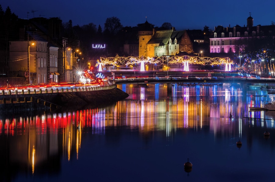 A nighttime cityscape with illuminated buildings, a bridge, and a river reflecting lights.