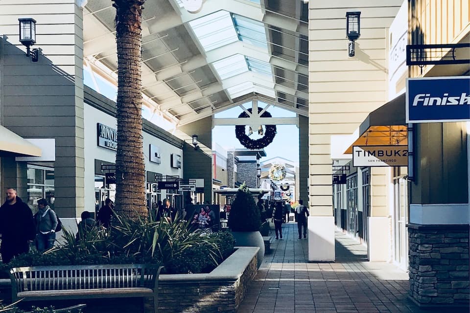 A shopping mall with a palm tree, benches, and a large archway.