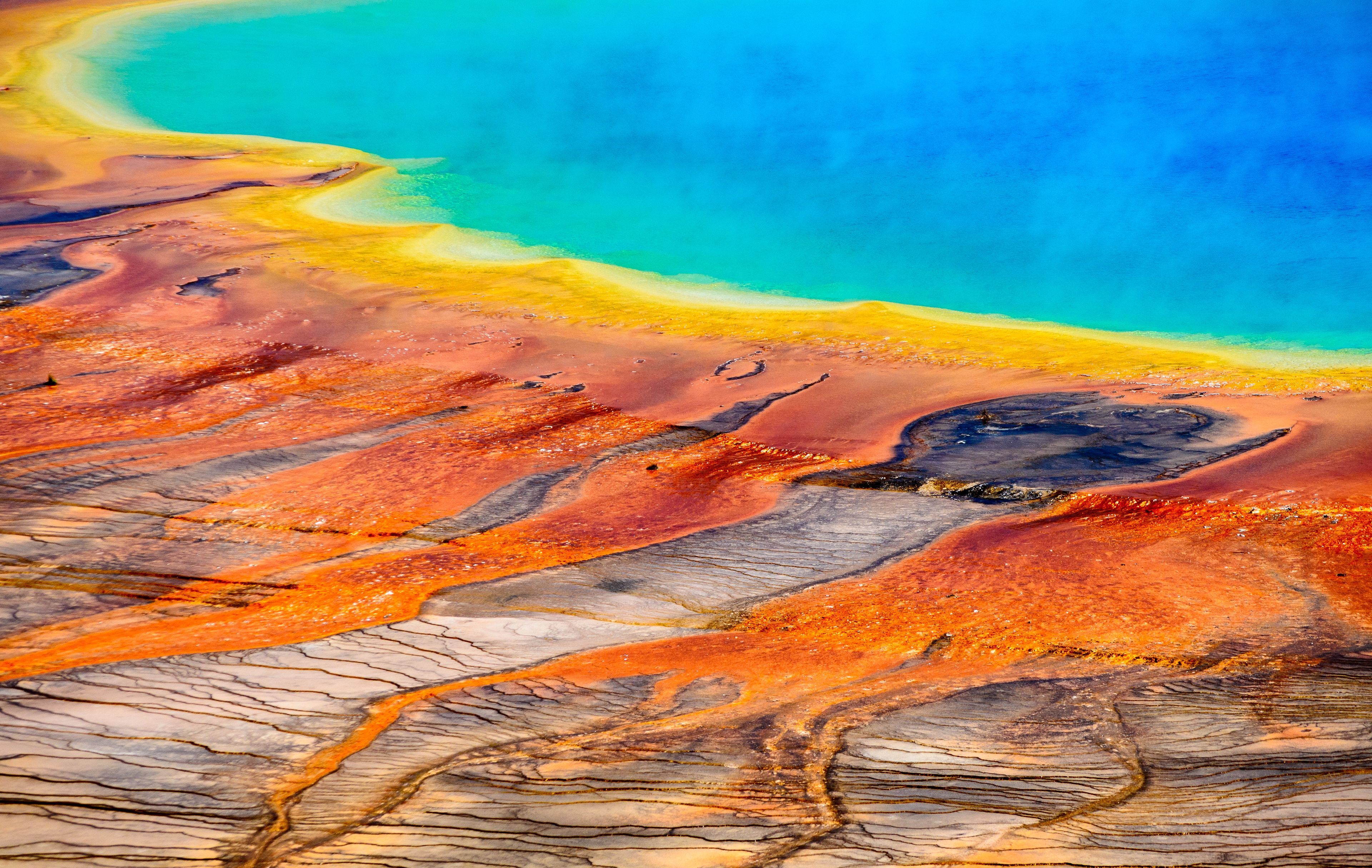 Paesaggio vivace con una distesa d'acqua turchese, una spiaggia sabbiosa e un terreno roccioso dai toni arancio e marroni.