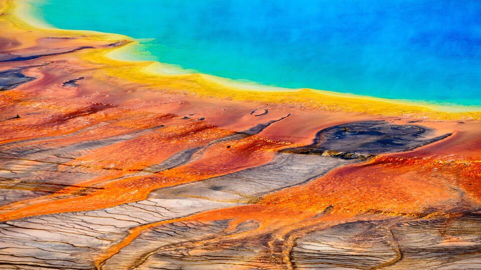 A vibrant landscape with a turquoise water body, a sandy beach, and a rocky terrain with orange and brown hues.