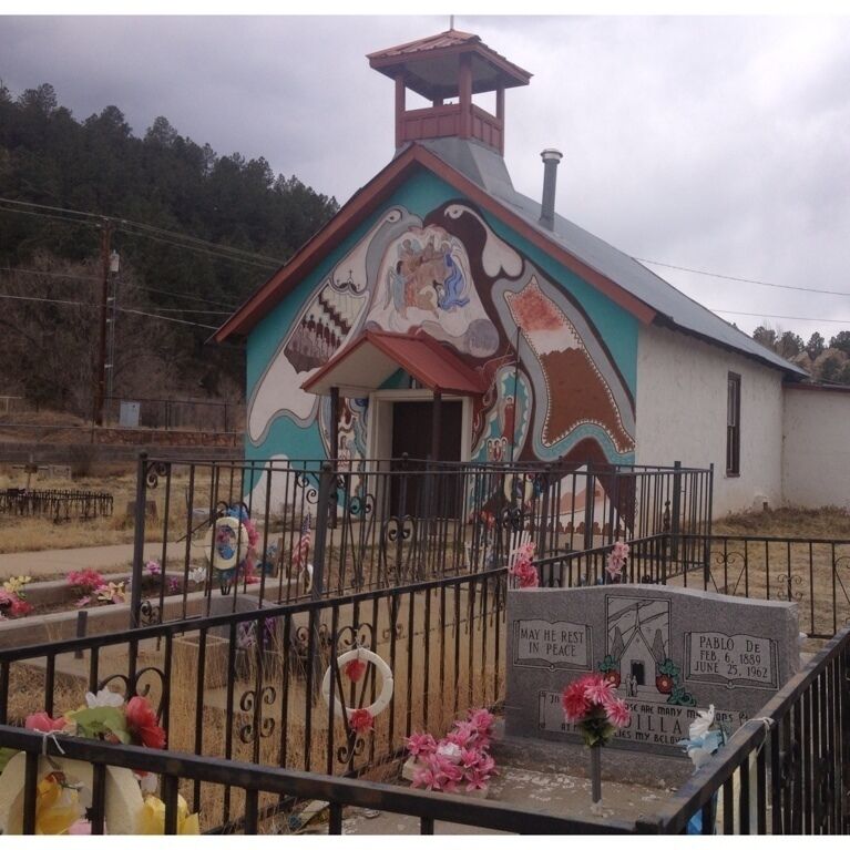 A church with colorful murals and a graveyard with flowers and a headstone.